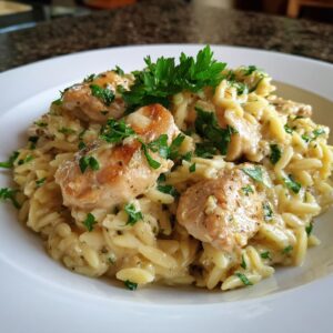 Close-up of creamy lemon chicken orzo topped with fresh parsley in a white bowl.