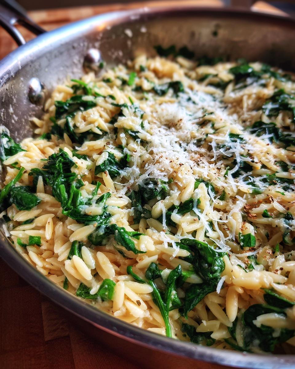 Close-up of creamy orzo pasta mixed with wilted spinach and topped with grated Parmesan cheese in a skillet.
