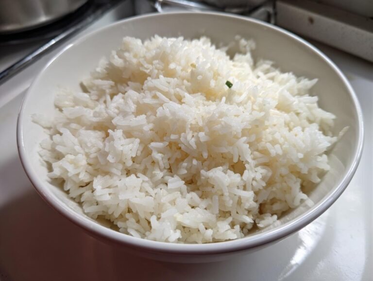 Close-up of fluffy, white cooked butter rice served in a simple white bowl, garnished with a tiny piece of green onion.