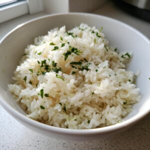 A close-up of fluffy white butter rice served in a white bowl and garnished with chopped green parsley.