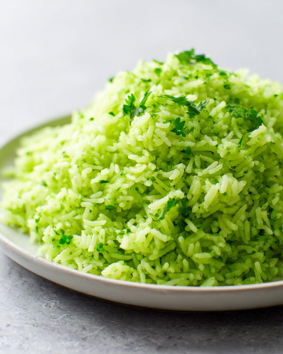 A close-up of fluffy, bright green cilantro lime rice mounded high on a light-colored plate.