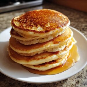 A tall stack of five golden brown, fluffy pancakes drizzled generously with maple syrup.