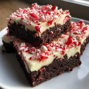 Close-up of fudgy peppermint brownies stacked, topped with thick white frosting and crushed candy canes.