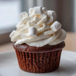 A close-up of a rich chocolate hot chocolate cupcake topped with swirled white frosting and mini marshmallows.