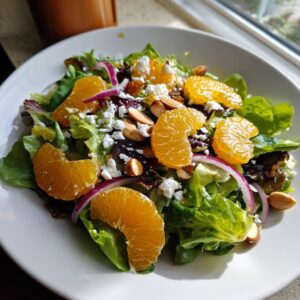 A bright mandarin orange salad featuring mixed greens, mandarin orange segments, feta cheese, and sliced almonds.