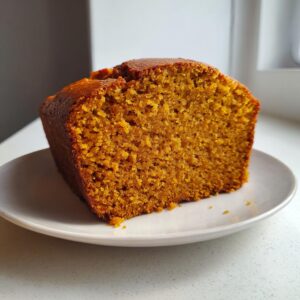 Close-up of a thick slice of moist pumpkin bread displaying its rich orange color and fine crumb texture.