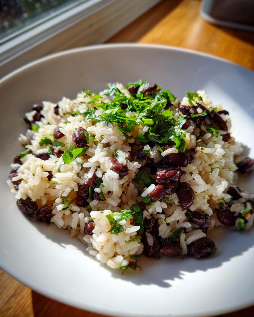 Close-up of a serving of fluffy white rice mixed with dark black beans and topped with fresh chopped cilantro.