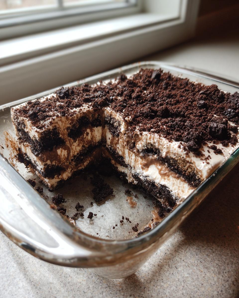 A creamy, layered Oreo dirt cake with a thick layer of crushed cookies on top, served in a clear glass baking dish.