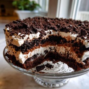 Cross-section view of a rich Oreo dirt cake showing layers of dark chocolate cake, white cream, and chocolate pudding, topped with crushed cookies.