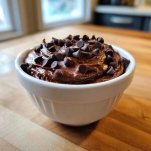 A white bowl filled with rich, glossy brownie batter dip, generously topped with mini chocolate chips.