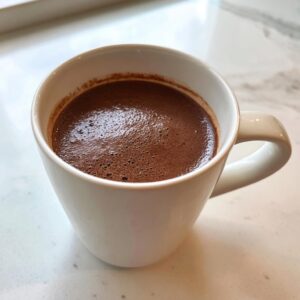 Close-up of a white mug filled with rich, dark hot chocolate topped with small bubbles.