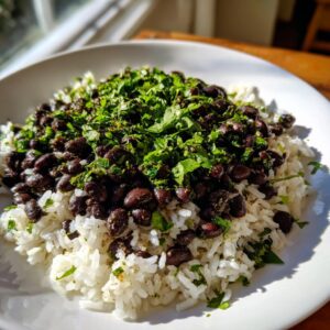 A close-up of fluffy white rice topped with seasoned black beans and a generous amount of fresh chopped cilantro, representing black beans and rice.