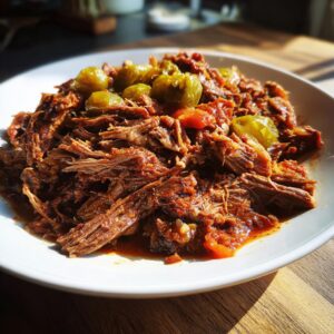A close-up of shredded Mississippi pot roast served on a white plate, topped with green pepperoncini peppers.