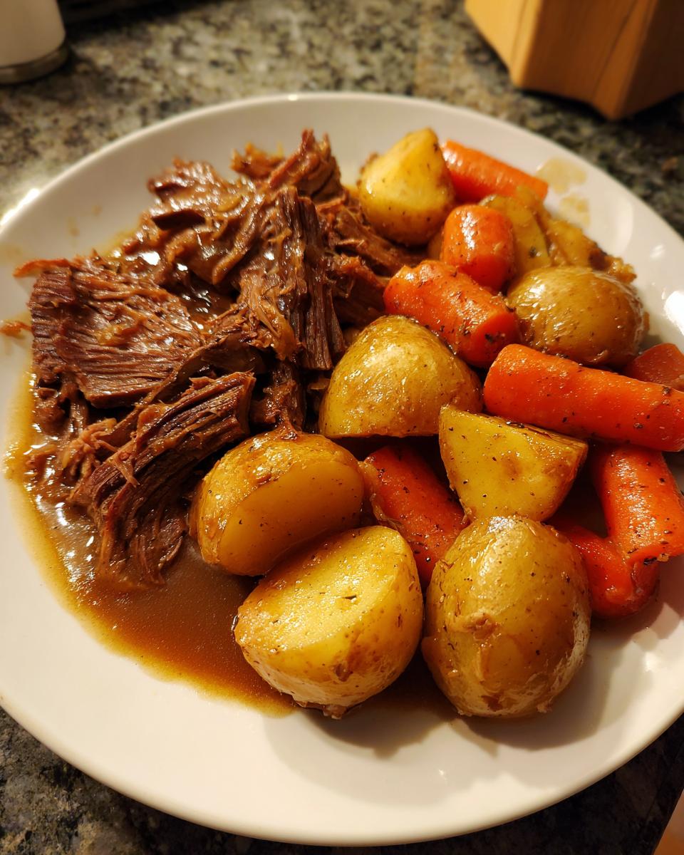 A plate of tender, shredded pot roast served with roasted carrots and small potatoes in rich gravy.