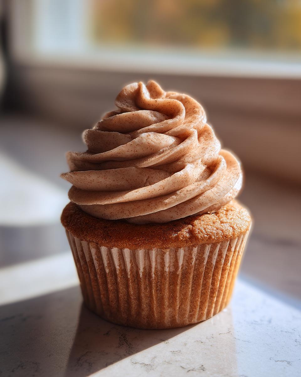 A single, perfectly baked banana cupcake topped with a tall swirl of light brown, spiced frosting.