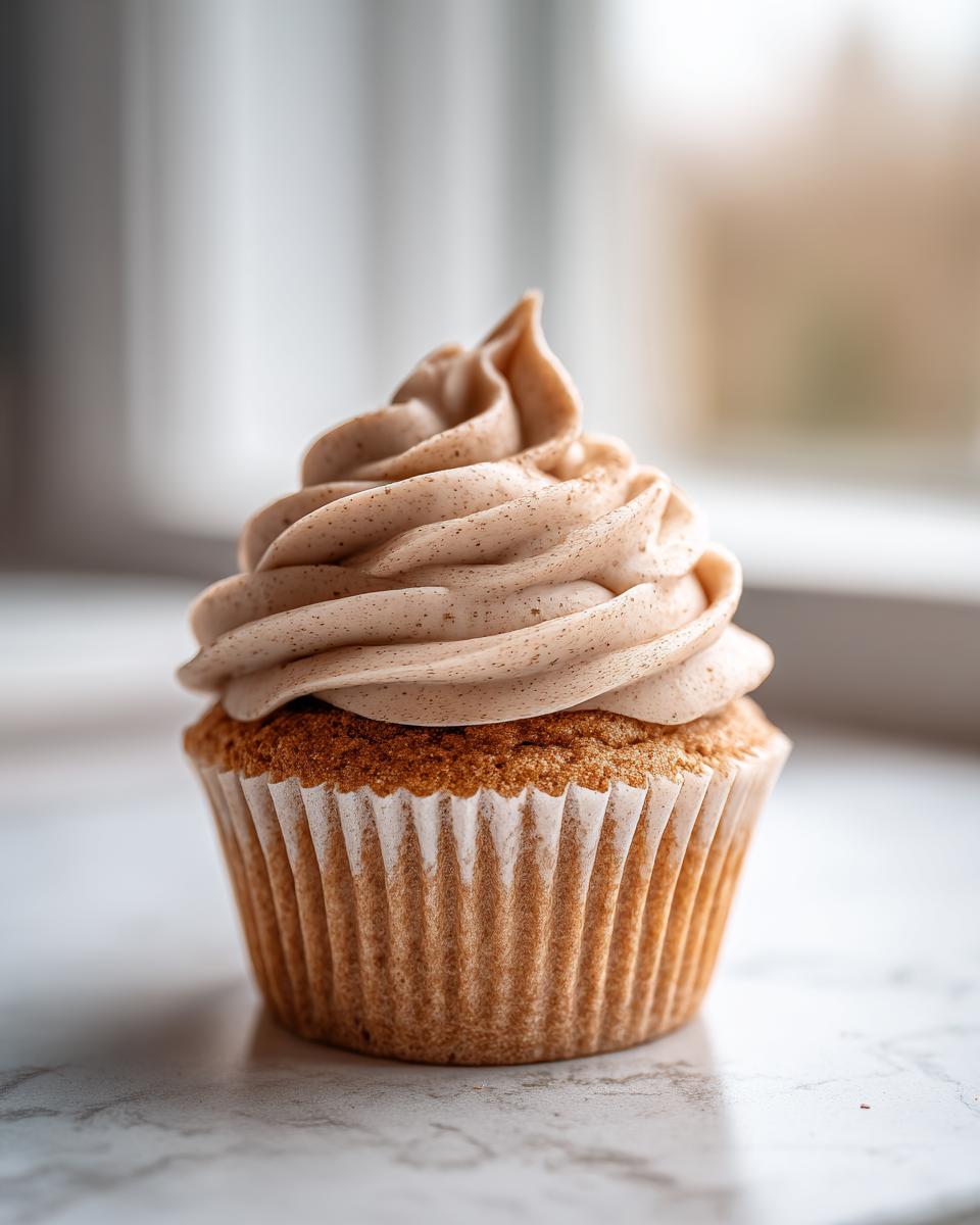 A single, perfectly baked banana cupcake topped with a tall swirl of light brown, speckled frosting.