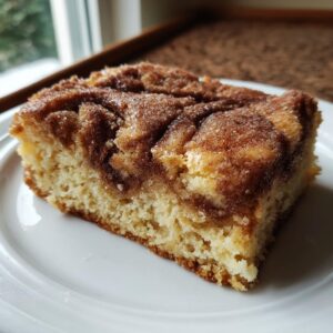 A moist square slice of snickerdoodle blondies with a rich cinnamon sugar swirl topping on a white plate.