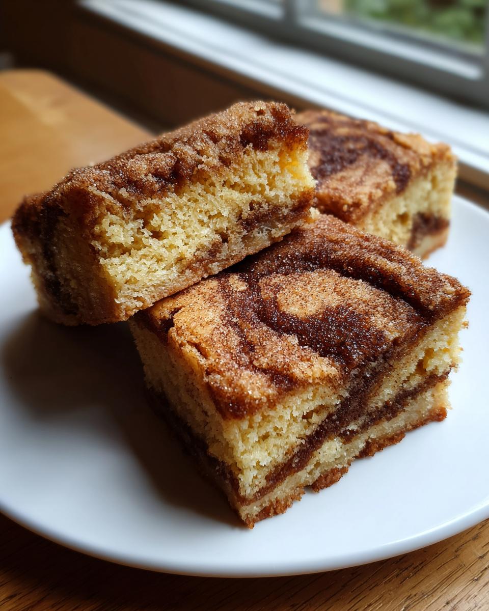 Three square slices of moist snickerdoodle blondies with a visible cinnamon swirl and sugary topping on a white plate.