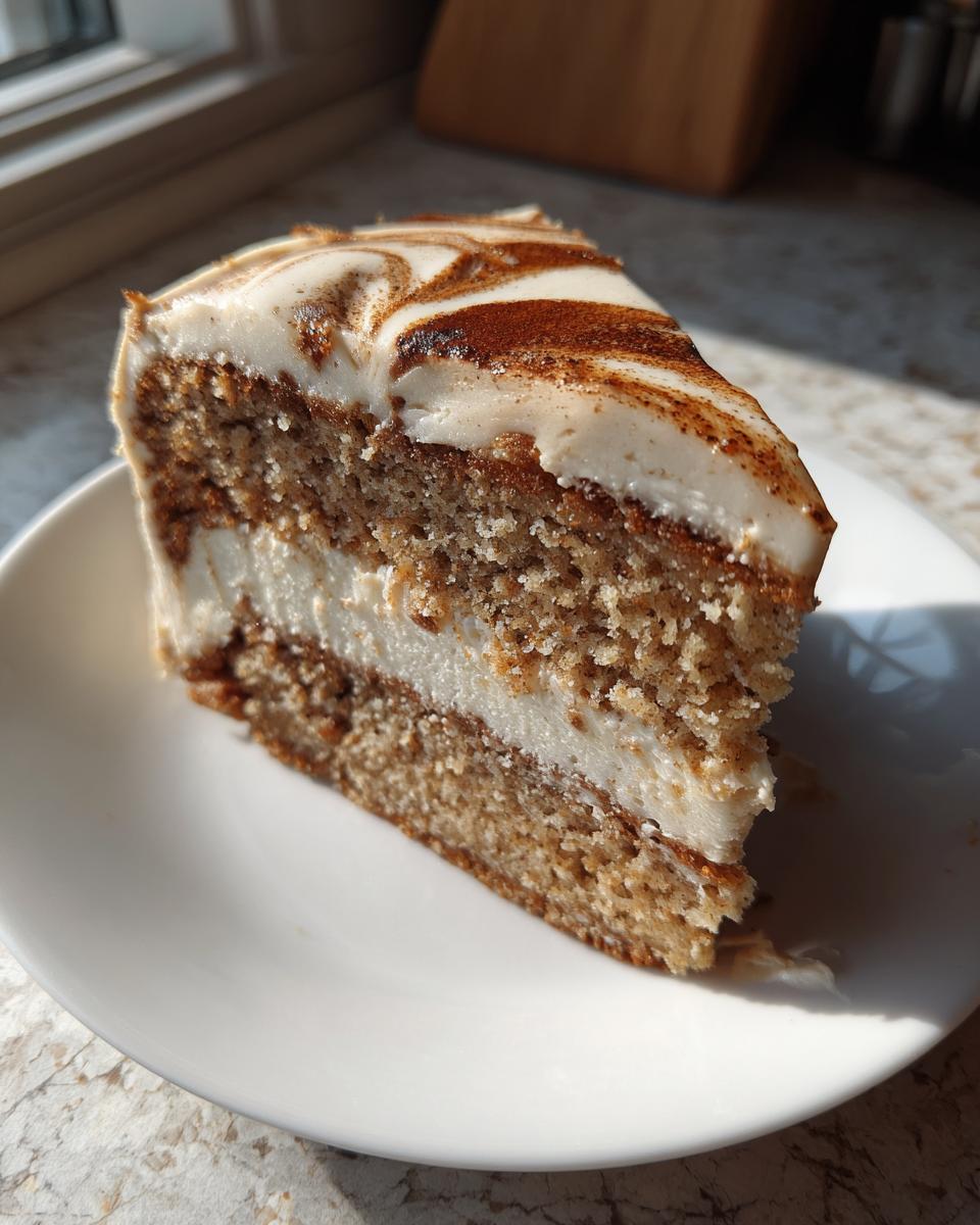 A close-up slice of moist spice cake layered with white frosting and cinnamon swirl topping.