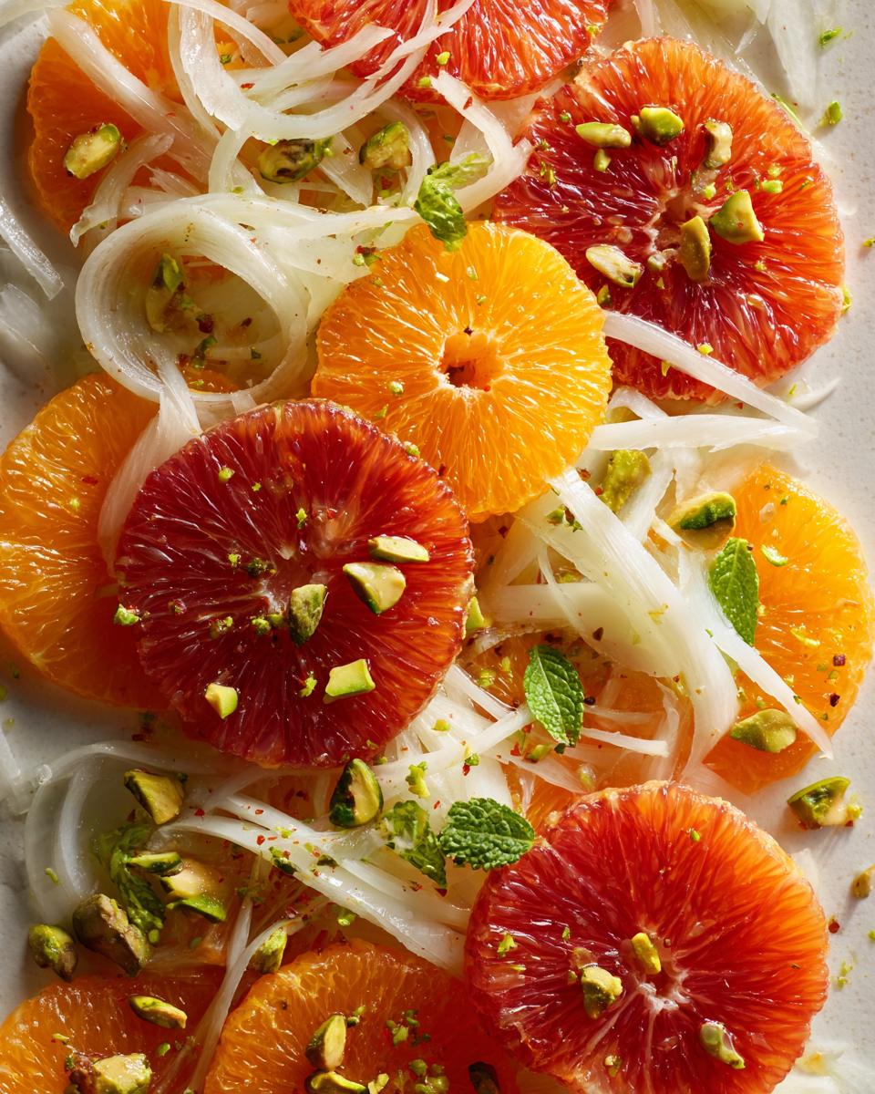 Close-up of a colorful citrus salad featuring slices of blood orange, navel orange, shaved fennel, pistachios, and mint.