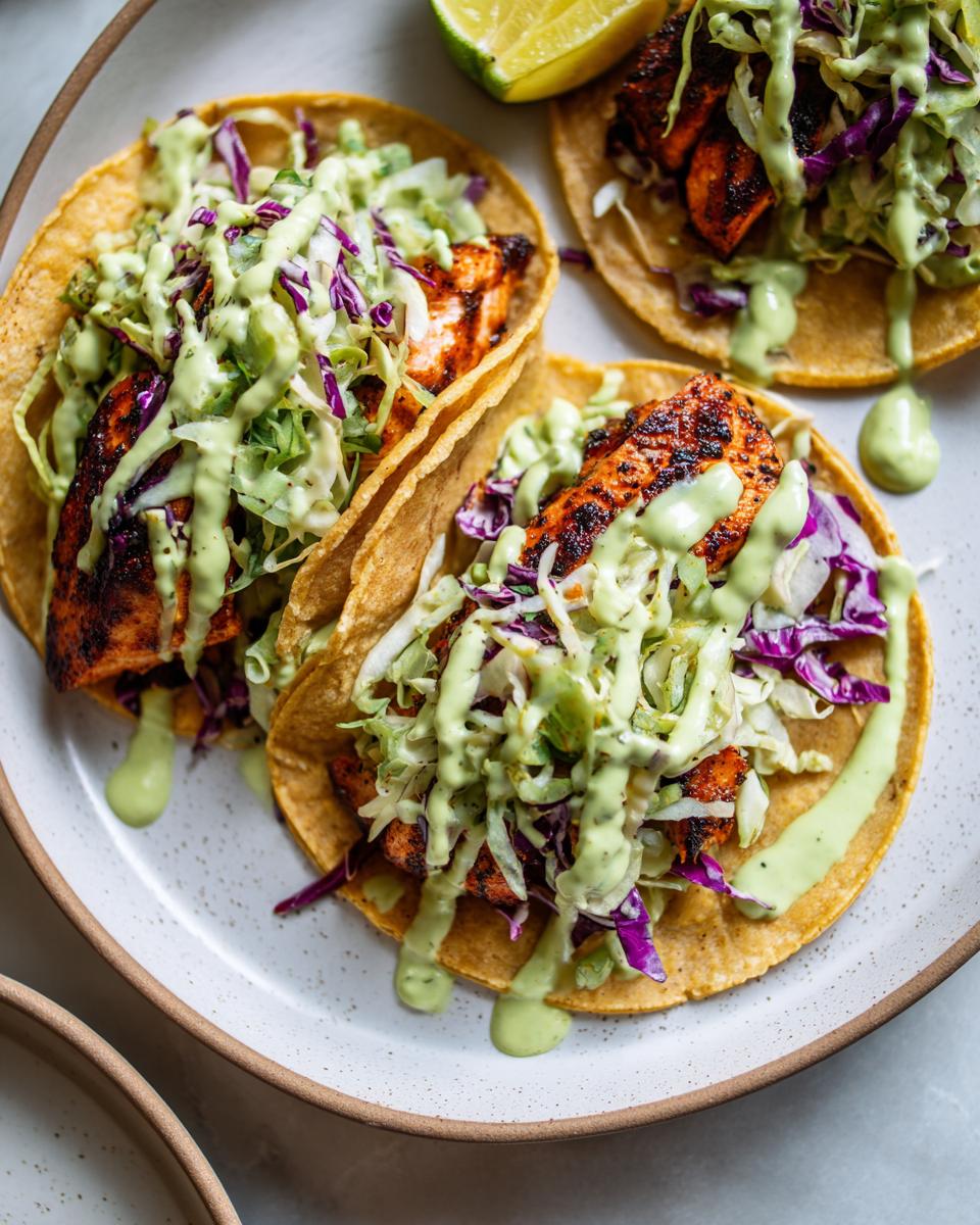 Three delicious salmon tacos topped with purple cabbage slaw and drizzled generously with a creamy green sauce.