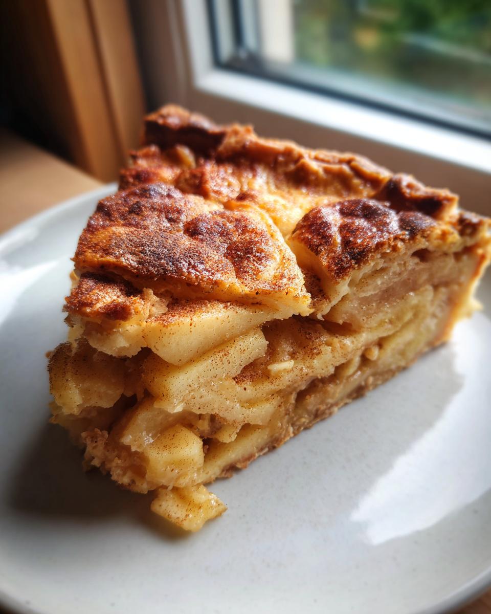 A close-up slice of amazing apple tart showing thick layers of spiced, cooked apples and a golden crust.