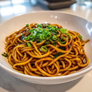 A close-up of glossy, saucy garlic noodles topped with fresh sliced green onions in a white bowl.