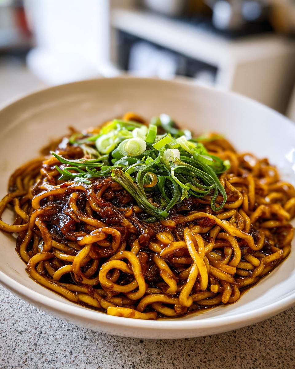 A close-up shot of a white bowl filled with glossy, dark sauce-coated garlic noodles, topped generously with fresh, sliced green onions.