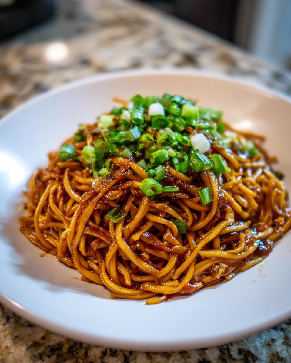 A close-up of a serving of glossy, saucy garlic noodles topped generously with fresh chopped green onions.