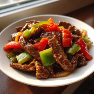 A close-up serving of glossy, saucy pepper steak with bright red and green bell peppers.