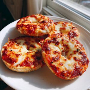 Four freshly baked pizza bagels topped with bubbling tomato sauce and melted mozzarella cheese on a white plate.