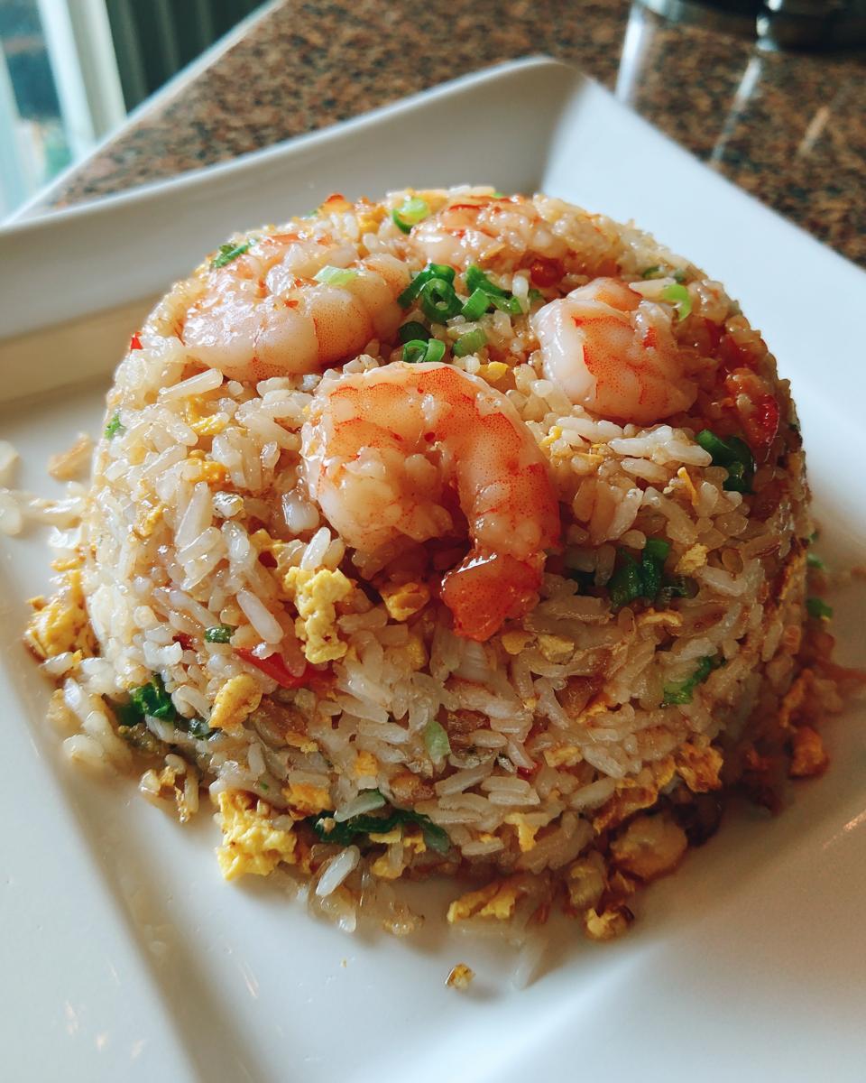 A molded mound of delicious shrimp fried rice topped with three large, pink shrimp and green onions.