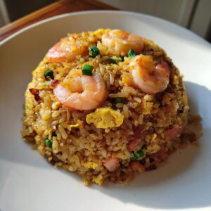 A mound of golden brown shrimp fried rice topped with four large pink shrimp and chopped green onions.