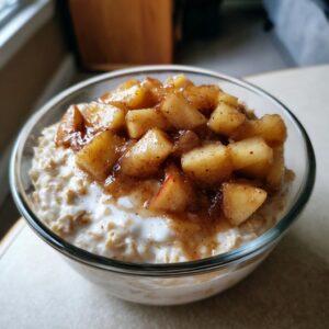Close-up of a glass bowl filled with creamy apple cinnamon oatmeal, topped generously with caramelized cinnamon apples.