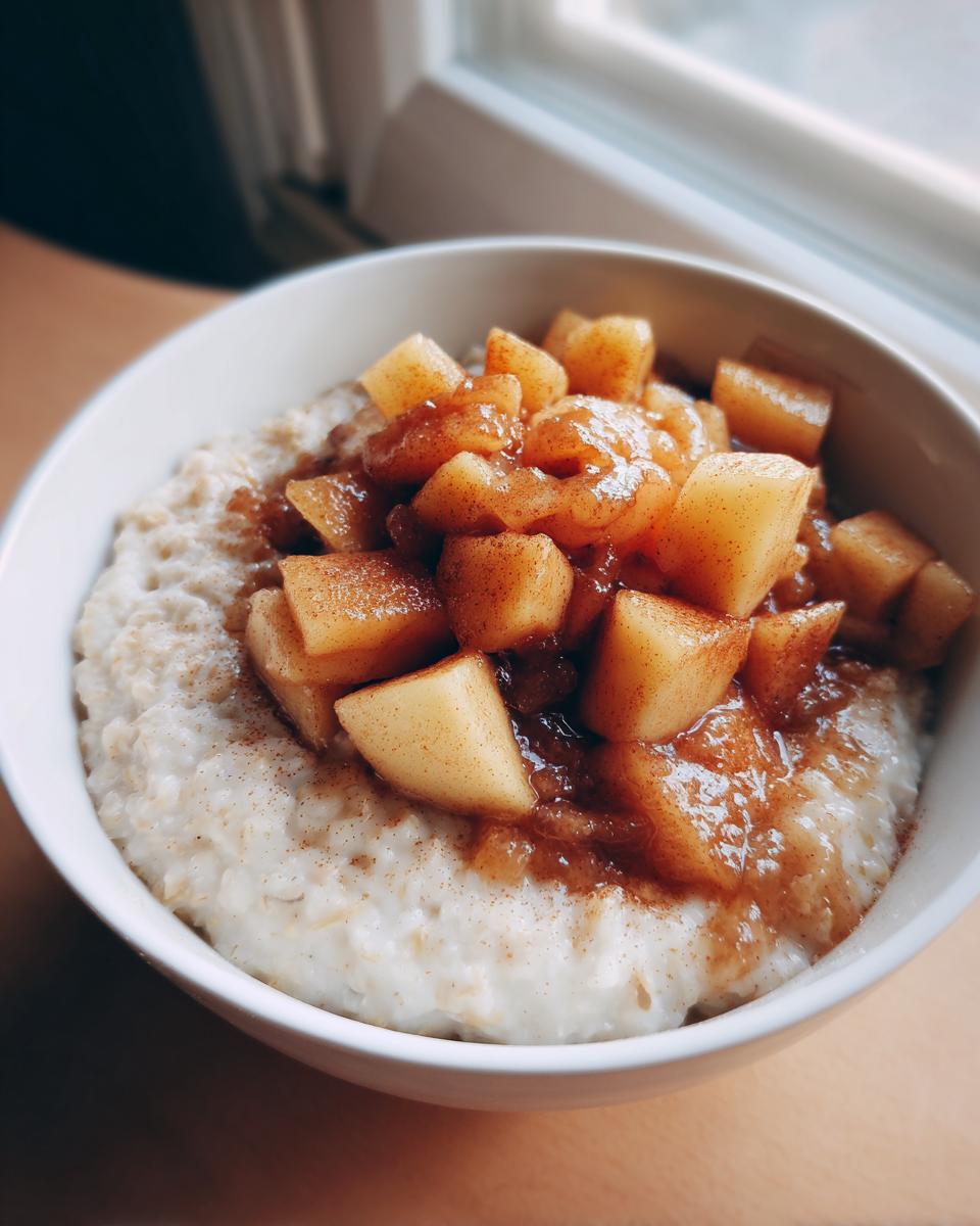 A close-up of a white bowl filled with creamy apple cinnamon oatmeal topped with caramelized apple chunks and cinnamon.
