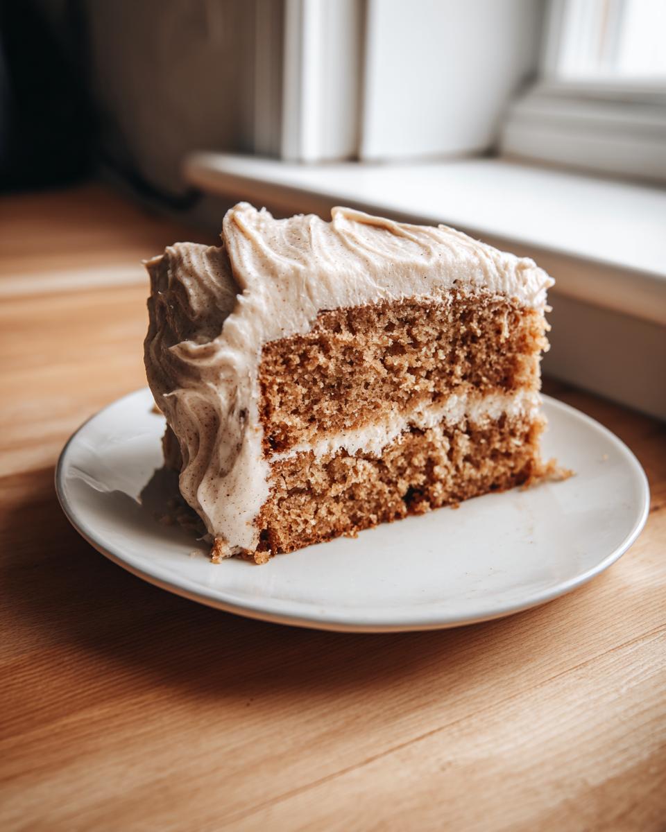 A moist slice of applesauce cake with two layers and thick, spiced frosting on a white plate.