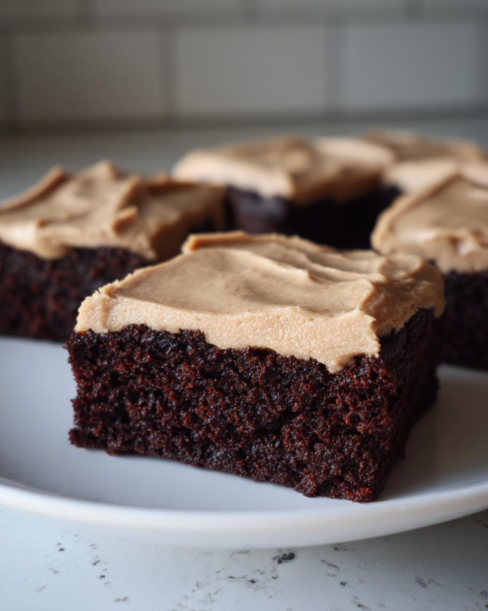 A close-up of a square of dark chocolate banana bread brownies topped with light brown frosting.