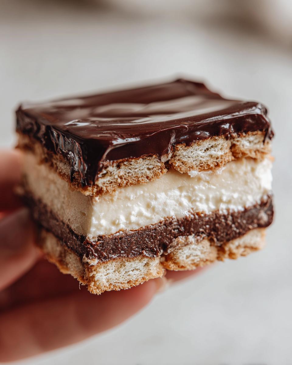 A close-up view of a square slice of chocolate eclair cake showing layers of vanilla cream, chocolate pudding, and graham crackers.