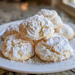 A stack of soft, crinkle-topped cool whip cookies heavily dusted with powdered sugar on a white plate.