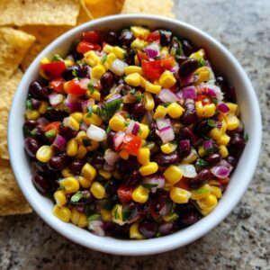 Close-up of fresh cowboy caviar featuring black beans, corn, red onion, and tomatoes, served with tortilla chips.