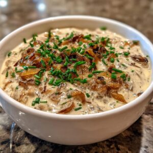 Close-up of a bowl of creamy caramelized onion dip topped with rich caramelized onions and fresh green chives.