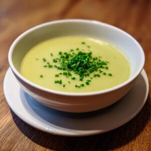 A close-up of a creamy, light green bowl of leek soup garnished generously with fresh chopped chives.