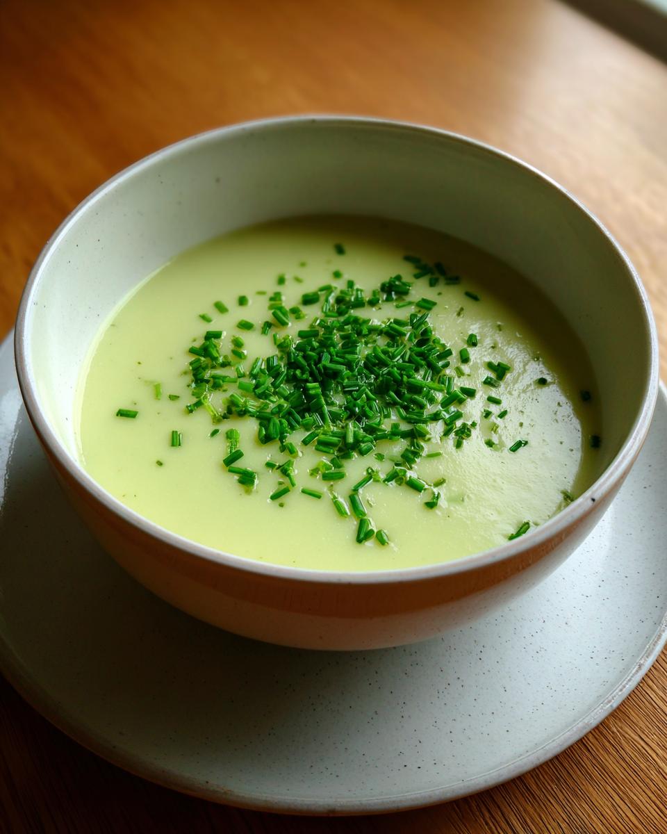 A close-up of a creamy, pale green bowl of leek soup topped generously with fresh, chopped chives.