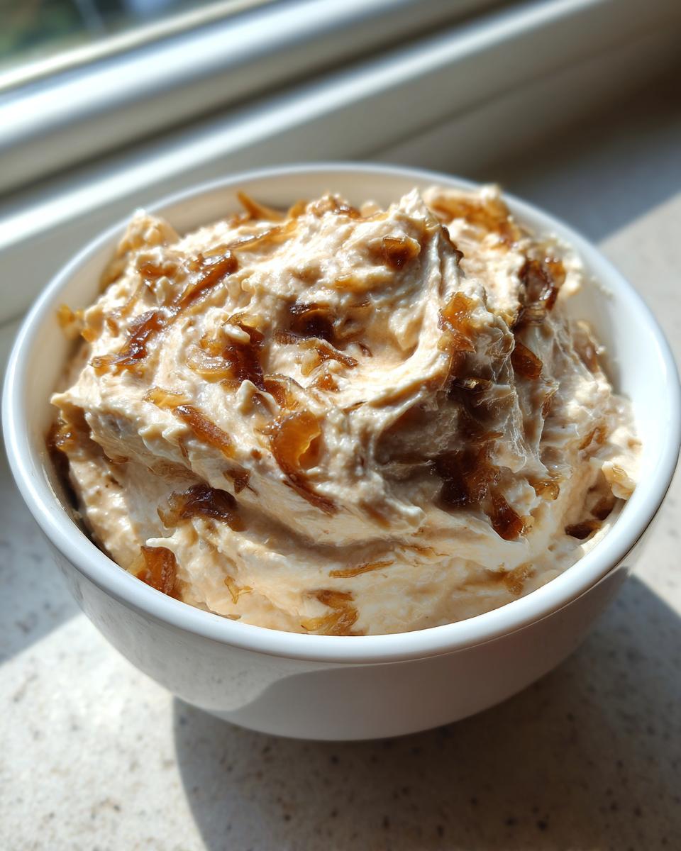 Close-up of a white bowl filled with creamy onion dip topped with caramelized onions.