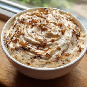 A white bowl filled with creamy homemade onion dip, swirled and topped generously with caramelized onions.