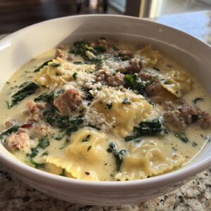 A close-up of a bowl of creamy ravioli soup featuring sausage crumbles, wilted spinach, and grated Parmesan cheese.