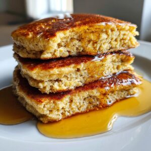 Close-up of a stack of three fluffy oatmeal pancakes cut in half, generously drizzled with golden syrup.