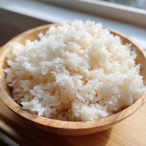 Close-up of perfectly cooked, fluffy white sushi rice piled high in a small wooden bowl.