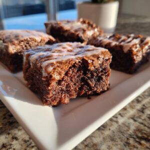 Close-up of fudgy gingerbread brownies squares topped with a white drizzle glaze on a white plate.
