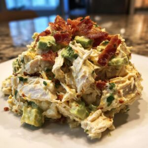 A mound of creamy honey mustard chicken salad mixed with avocado chunks and topped with crispy bacon bits.